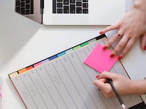 a woman writing tasks in a neatly organized notebook. Her list of tasks and events read: 'Team, Process, Planning, IT, Studio'.