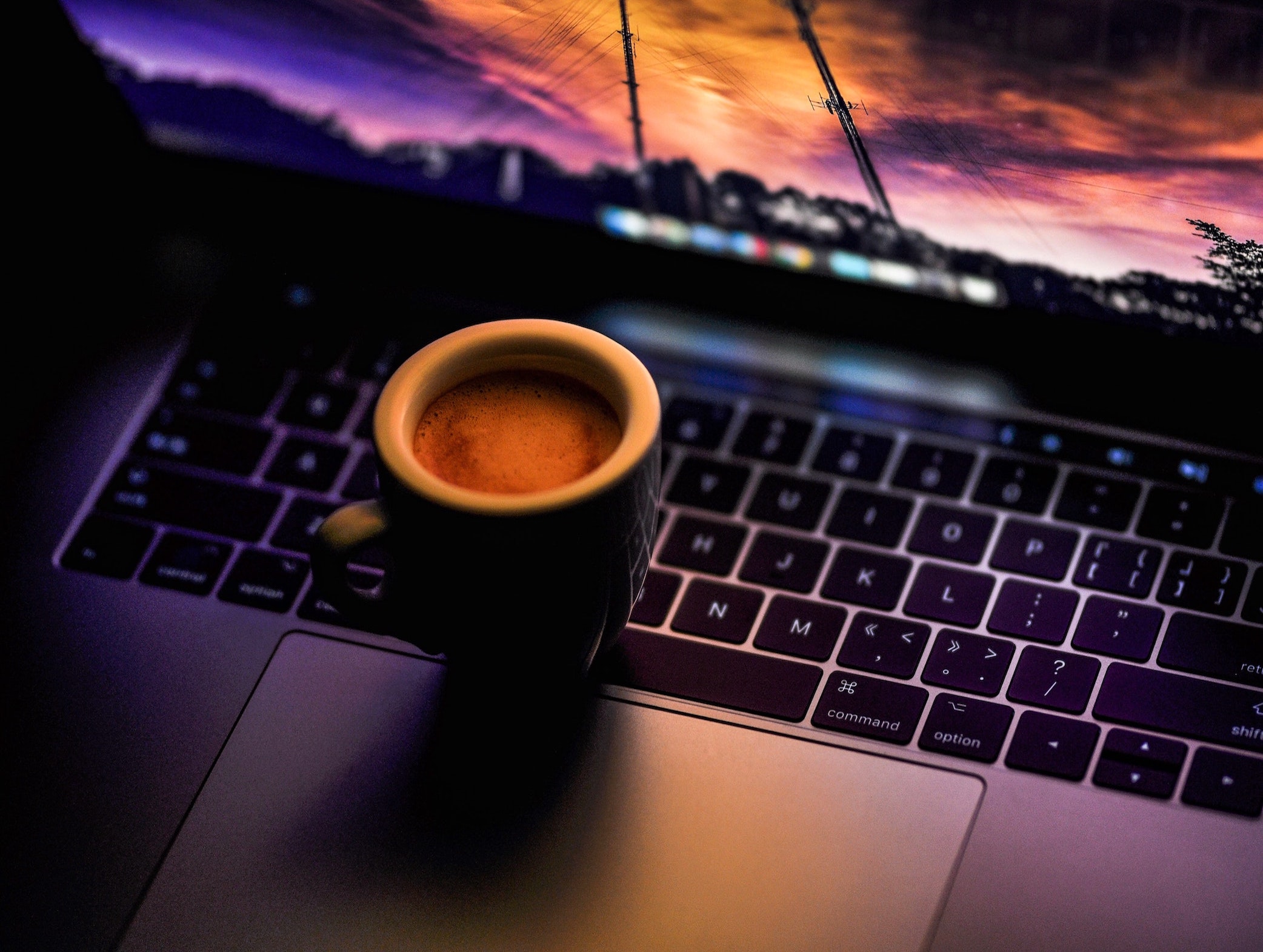 a tiny espresso filled cup resting on a macbook keyboard.